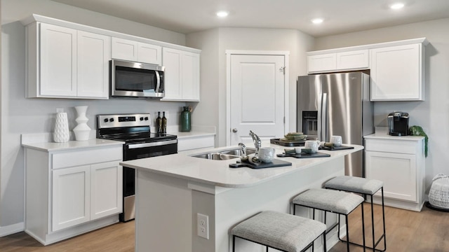 kitchen with stainless steel appliances, light hardwood / wood-style floors, a kitchen breakfast bar, a kitchen island with sink, and white cabinets