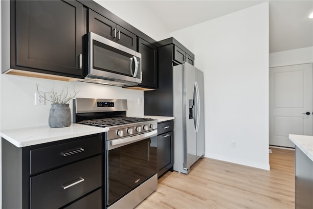 kitchen with stainless steel appliances, light stone countertops, and light hardwood / wood-style flooring