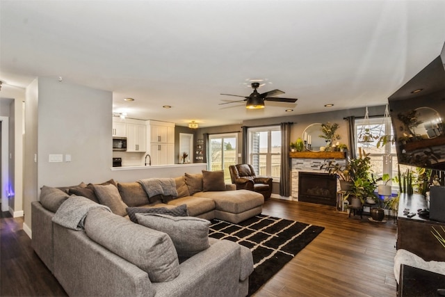 living room featuring dark wood-type flooring, sink, ceiling fan, and a fireplace