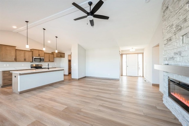 kitchen with appliances with stainless steel finishes, brown cabinetry, open floor plan, light wood-style floors, and a stone fireplace