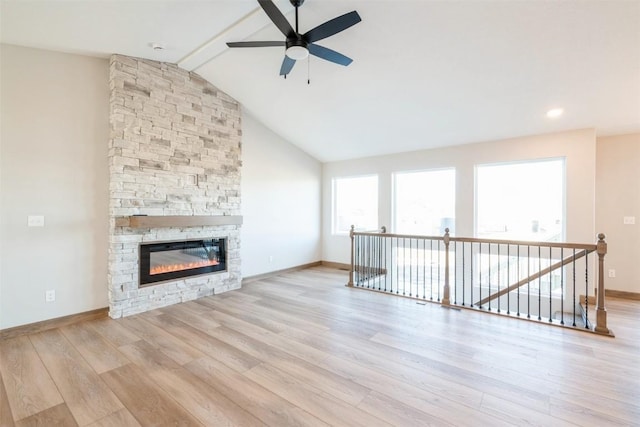 unfurnished living room with a stone fireplace, lofted ceiling with beams, ceiling fan, and light wood-type flooring