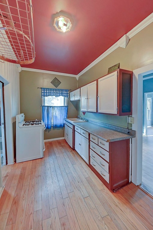 kitchen with white gas stove, white cabinetry, light wood-type flooring, and crown molding