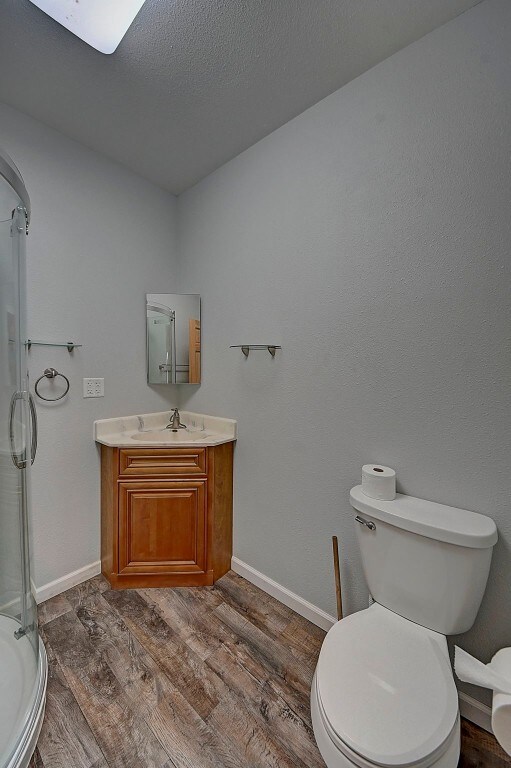 bathroom featuring wood-type flooring, vanity, toilet, and a shower with shower door