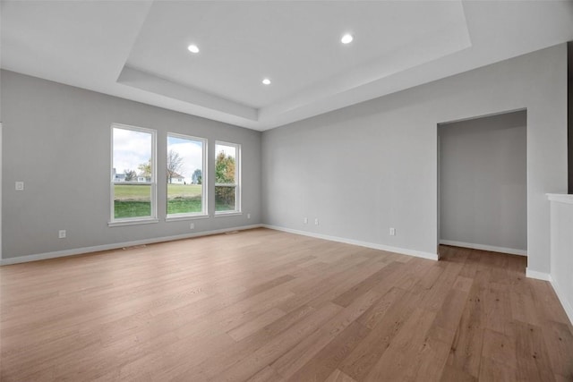 spare room featuring a tray ceiling and light wood-type flooring