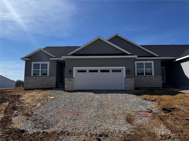 craftsman house with an attached garage, stone siding, and driveway