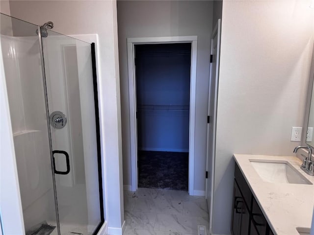 bathroom with marble finish floor, a stall shower, vanity, baseboards, and a spacious closet