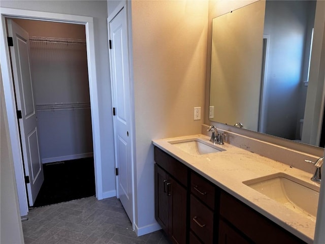 full bath featuring a sink, a walk in closet, baseboards, and double vanity