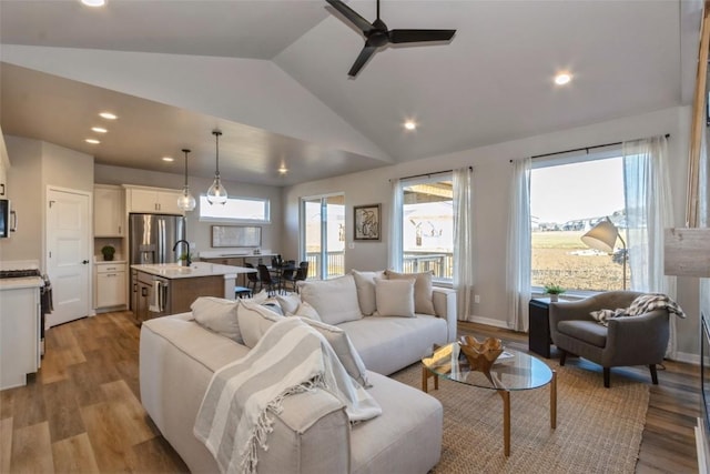 living room with ceiling fan, sink, light hardwood / wood-style flooring, and vaulted ceiling