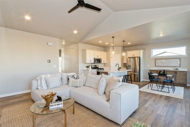 living room featuring ceiling fan, light wood-type flooring, and vaulted ceiling