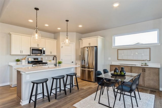 kitchen featuring stainless steel appliances, decorative light fixtures, a center island with sink, light hardwood / wood-style flooring, and white cabinetry