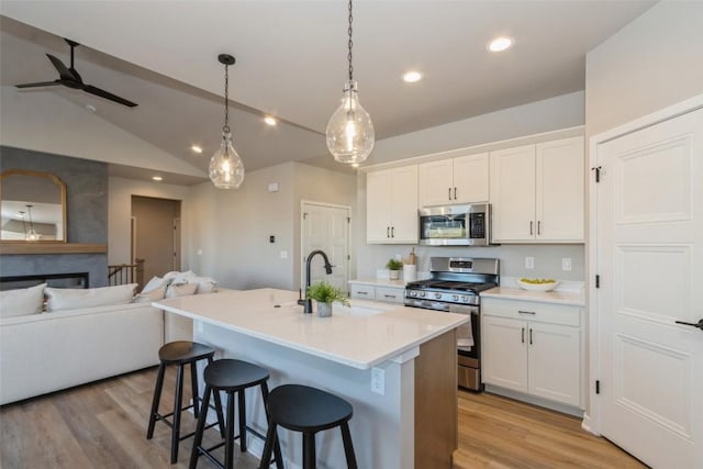 kitchen with stainless steel appliances, white cabinetry, lofted ceiling, and an island with sink