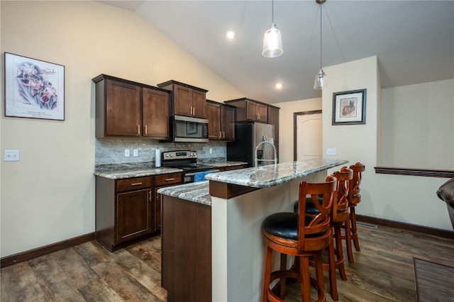 kitchen featuring stainless steel appliances, light stone counters, vaulted ceiling, a breakfast bar, and pendant lighting