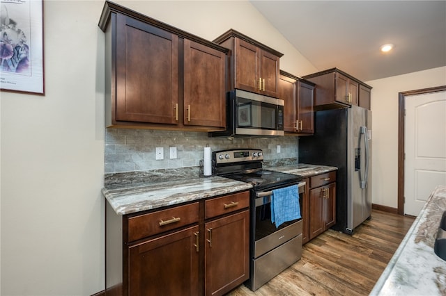 kitchen with stainless steel appliances, hardwood / wood-style flooring, backsplash, and light stone countertops