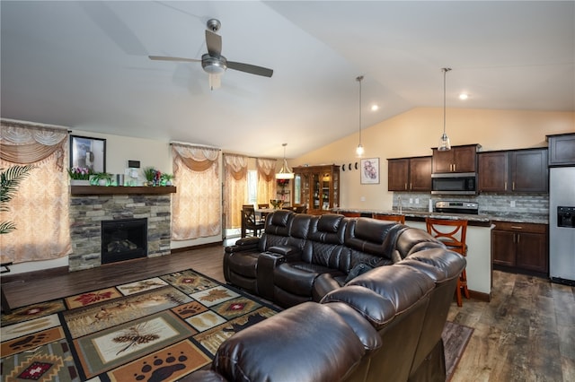 living room with dark hardwood / wood-style flooring, a stone fireplace, vaulted ceiling, and ceiling fan