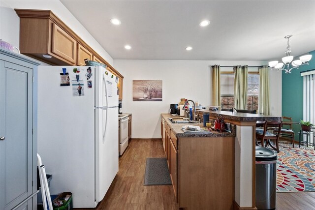 kitchen with sink, dark hardwood / wood-style floors, a kitchen bar, decorative light fixtures, and white appliances