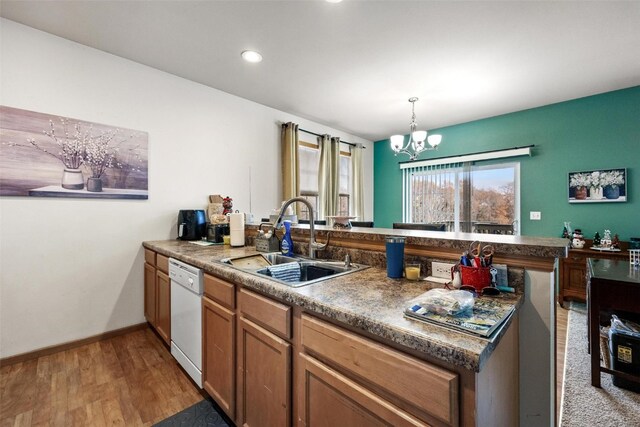 kitchen with white dishwasher, kitchen peninsula, a notable chandelier, sink, and light hardwood / wood-style flooring