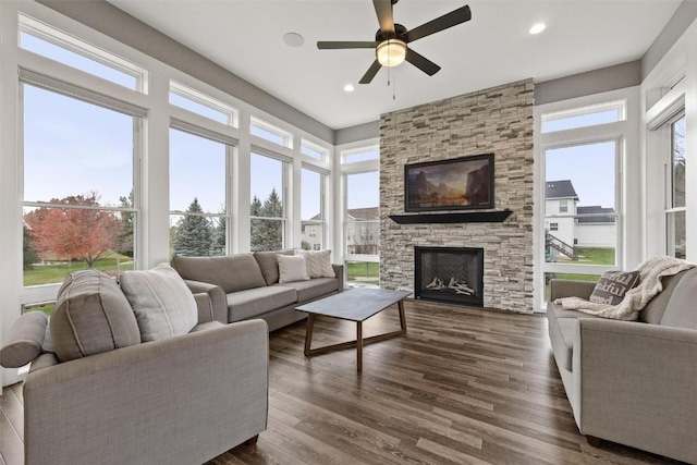 living room with ceiling fan, dark wood-type flooring, and a stone fireplace