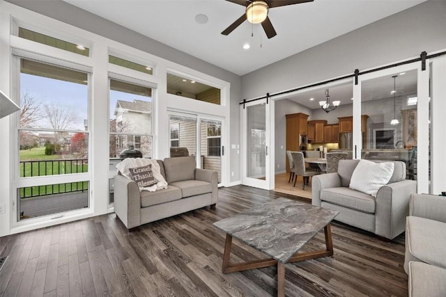 living room with ceiling fan with notable chandelier, dark hardwood / wood-style floors, a barn door, and vaulted ceiling