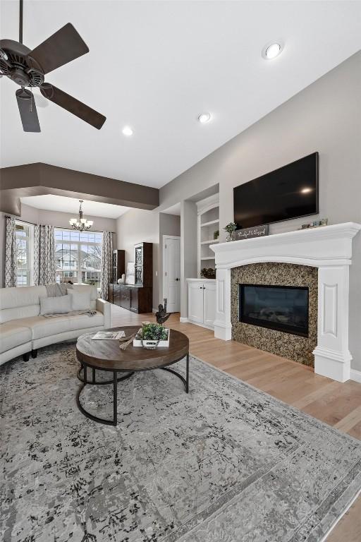 living room with built in features, light wood-type flooring, and ceiling fan with notable chandelier