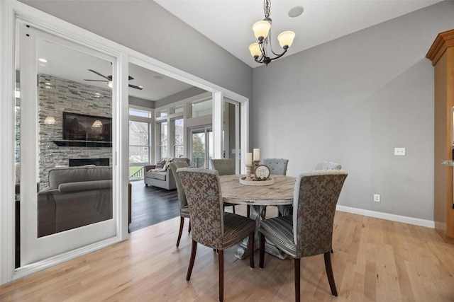 dining space with ceiling fan with notable chandelier, a stone fireplace, and light wood-type flooring