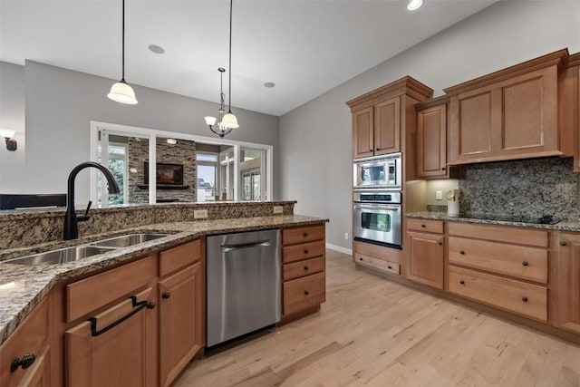 kitchen with appliances with stainless steel finishes, tasteful backsplash, hanging light fixtures, sink, and light hardwood / wood-style flooring