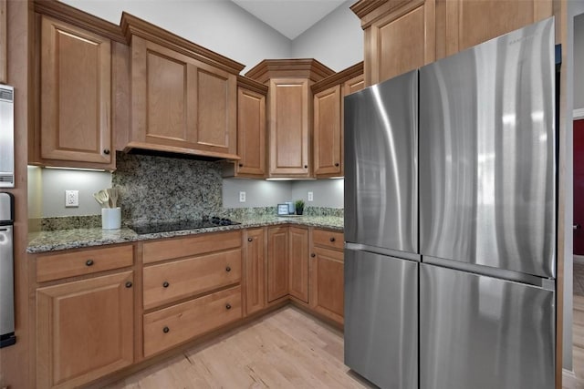 kitchen with stainless steel fridge, backsplash, black electric stovetop, light stone counters, and light hardwood / wood-style floors