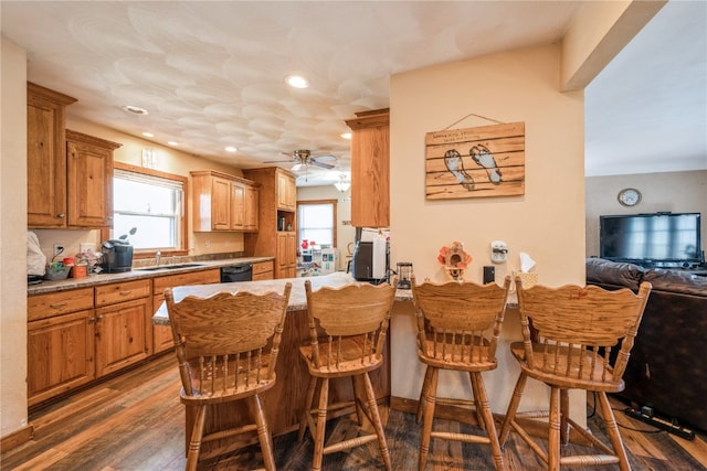 kitchen with a kitchen bar, kitchen peninsula, ceiling fan, dark wood-type flooring, and dishwasher