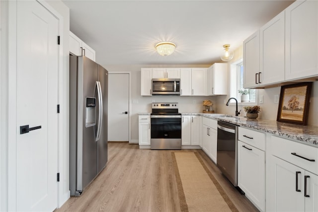 kitchen featuring stainless steel appliances, light stone counters, sink, white cabinetry, and light hardwood / wood-style flooring