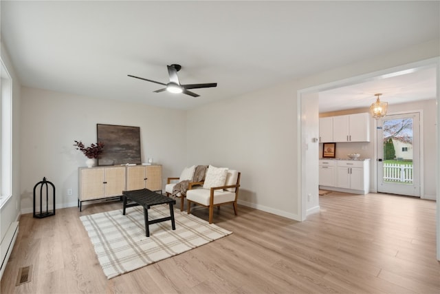 living area featuring baseboard heating, ceiling fan with notable chandelier, and light hardwood / wood-style floors