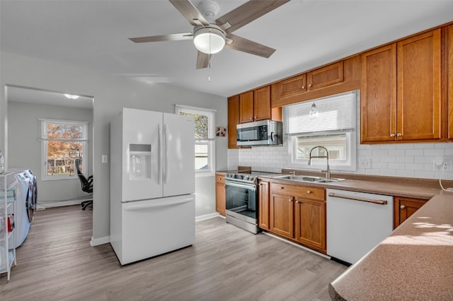 kitchen featuring separate washer and dryer, stainless steel appliances, sink, backsplash, and light wood-type flooring