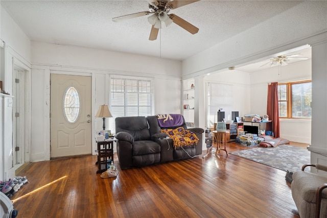 living room with a textured ceiling, dark hardwood / wood-style floors, ceiling fan, and decorative columns