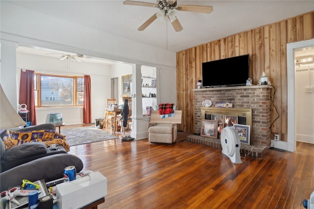 living room featuring wood-type flooring, a fireplace, a textured ceiling, wooden walls, and ceiling fan