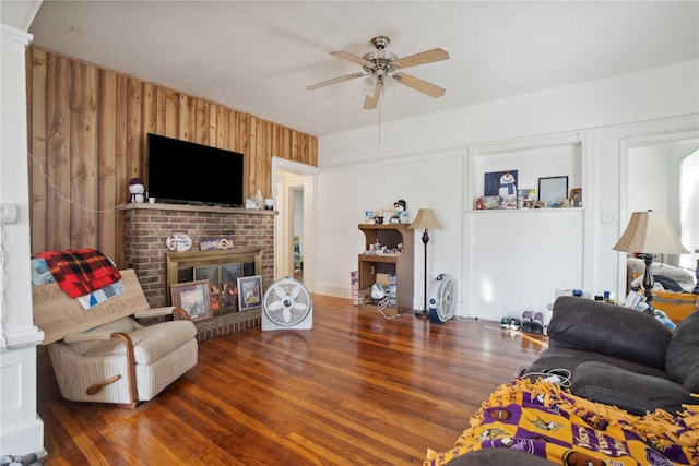 living room featuring a textured ceiling, a fireplace, dark wood-type flooring, and ceiling fan