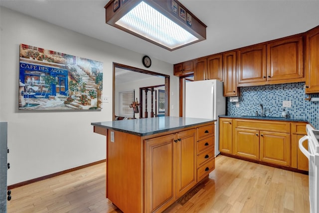 kitchen featuring light wood-type flooring, tasteful backsplash, white appliances, sink, and a kitchen island