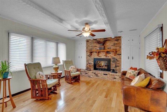 living room with beam ceiling, ceiling fan, a brick fireplace, light hardwood / wood-style flooring, and a textured ceiling