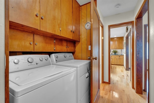 clothes washing area featuring washing machine and dryer, cabinets, and light wood-type flooring