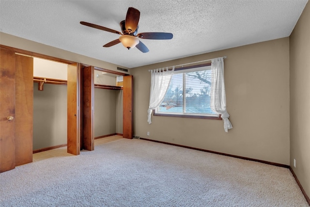 unfurnished bedroom with ceiling fan, a textured ceiling, light carpet, and multiple closets