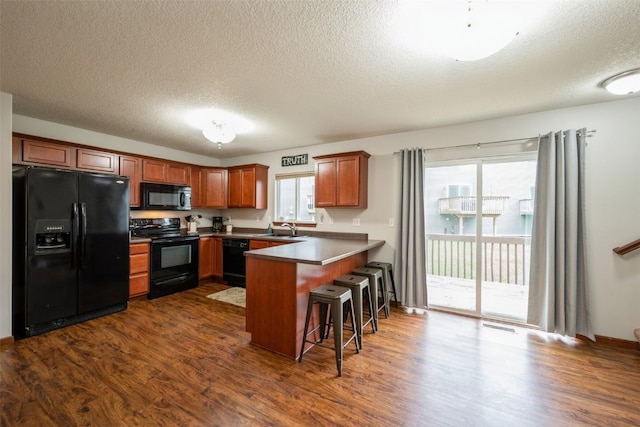 kitchen with sink, dark wood-type flooring, a kitchen breakfast bar, kitchen peninsula, and black appliances