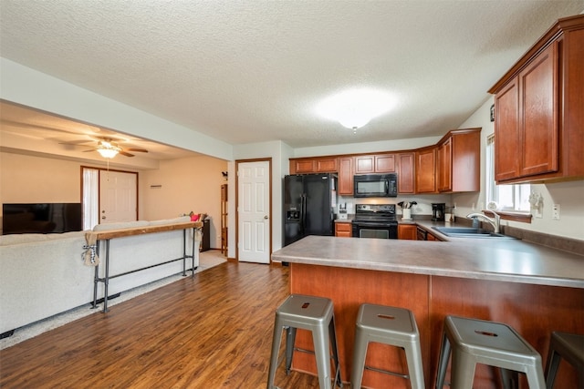 kitchen featuring sink, dark hardwood / wood-style floors, a textured ceiling, a breakfast bar area, and black appliances