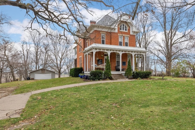 view of front of home with an outbuilding, covered porch, a front yard, and a garage