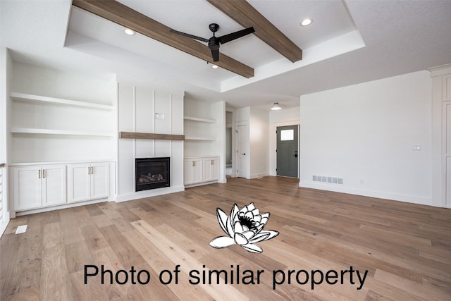 unfurnished living room featuring ceiling fan, light wood-type flooring, a textured ceiling, built in features, and a large fireplace