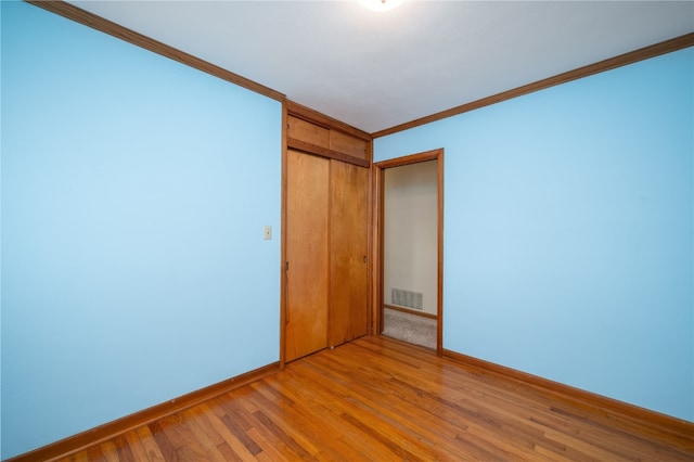 unfurnished bedroom with crown molding, a closet, and light wood-type flooring