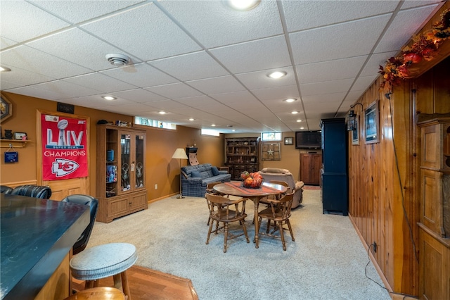 dining space featuring carpet flooring, a paneled ceiling, and wood walls