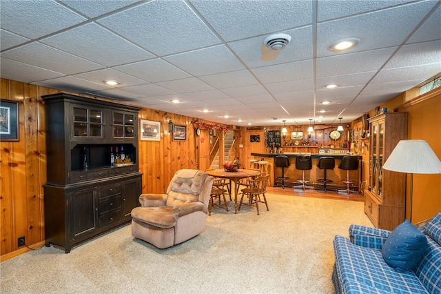 carpeted living room featuring bar area, a paneled ceiling, and wooden walls