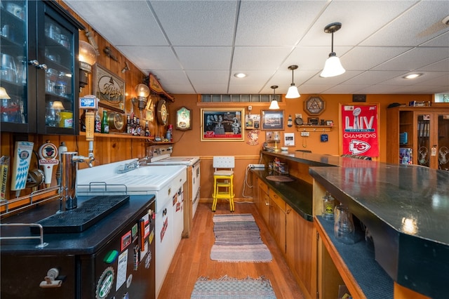 bar featuring a paneled ceiling, decorative light fixtures, and light hardwood / wood-style flooring