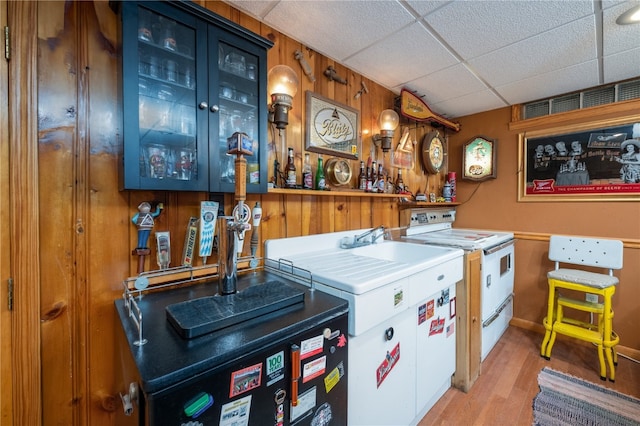 bar featuring washing machine and clothes dryer, white electric range oven, wood walls, a paneled ceiling, and light wood-type flooring