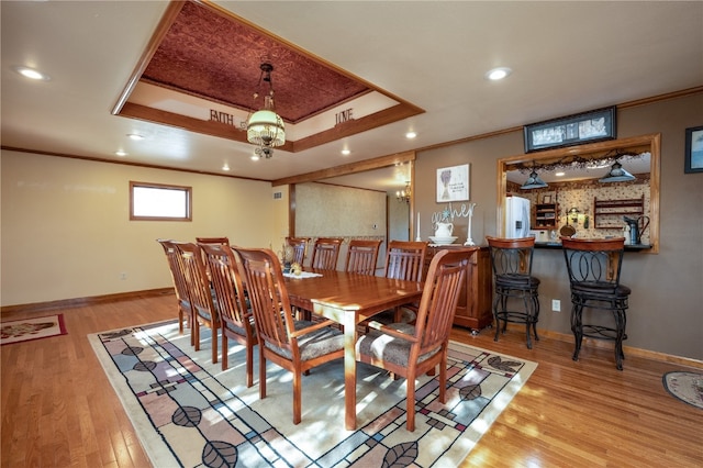 dining space featuring a notable chandelier, a raised ceiling, light wood-type flooring, and crown molding