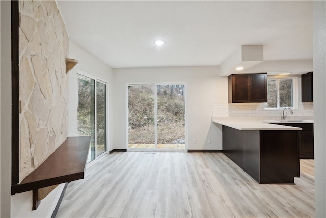 kitchen with kitchen peninsula, tasteful backsplash, dark brown cabinetry, sink, and light hardwood / wood-style flooring