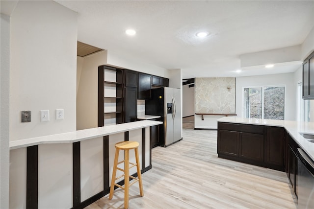 kitchen featuring a breakfast bar, light wood-type flooring, appliances with stainless steel finishes, dark brown cabinets, and kitchen peninsula