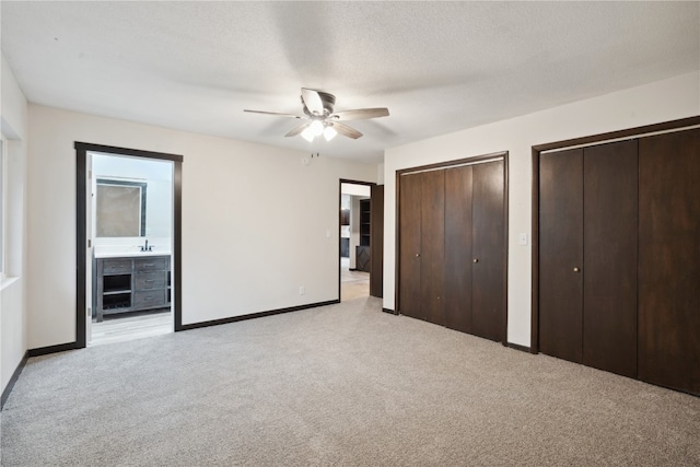 unfurnished bedroom featuring multiple closets, ceiling fan, ensuite bathroom, a textured ceiling, and light carpet